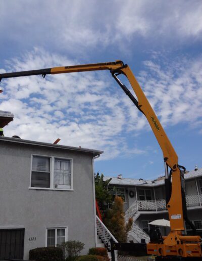A crane lifts roofing materials to workers on the roof of a two-story apartment building under a partly cloudy sky.